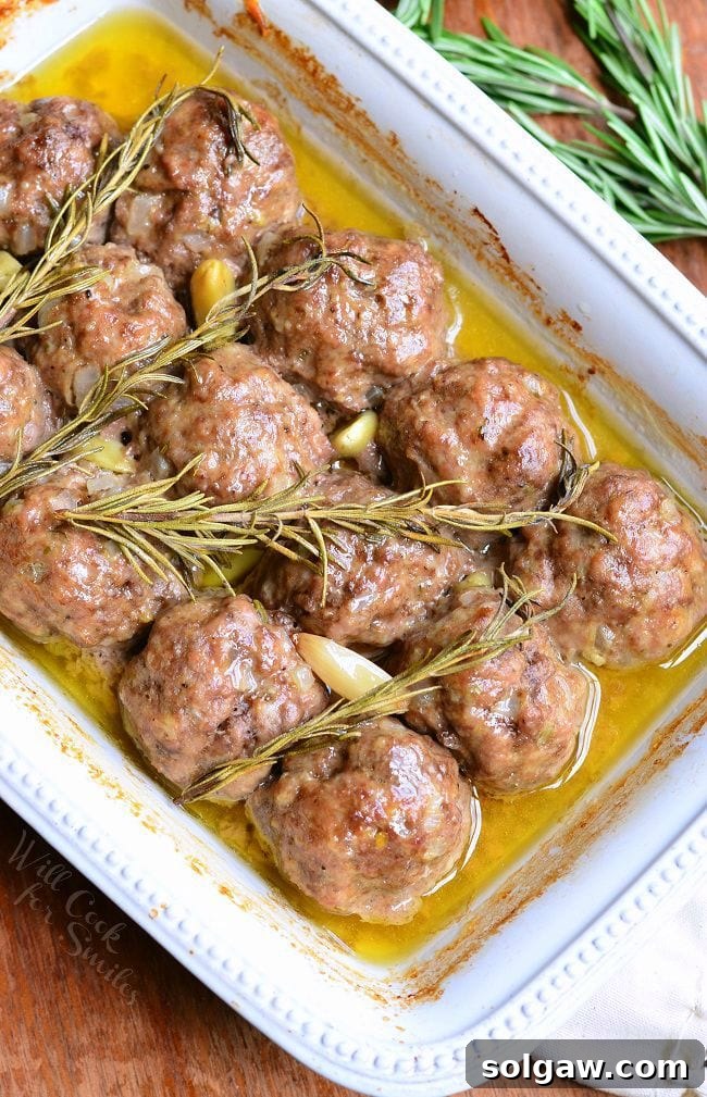 Top view of Rosemary Garlic Baked Meatballs in a white baking dish with rosemary and pieces of garlic after being cooked.