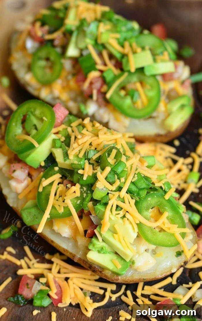 Zesty Fiesta Chicken Stuffed Potatoes 3 A vibrant top-down view of two Fiesta Chicken Twice Baked Potatoes, generously garnished with a colorful medley of cheese, fresh green onions, sliced jalapenos, and creamy avocado cubes.