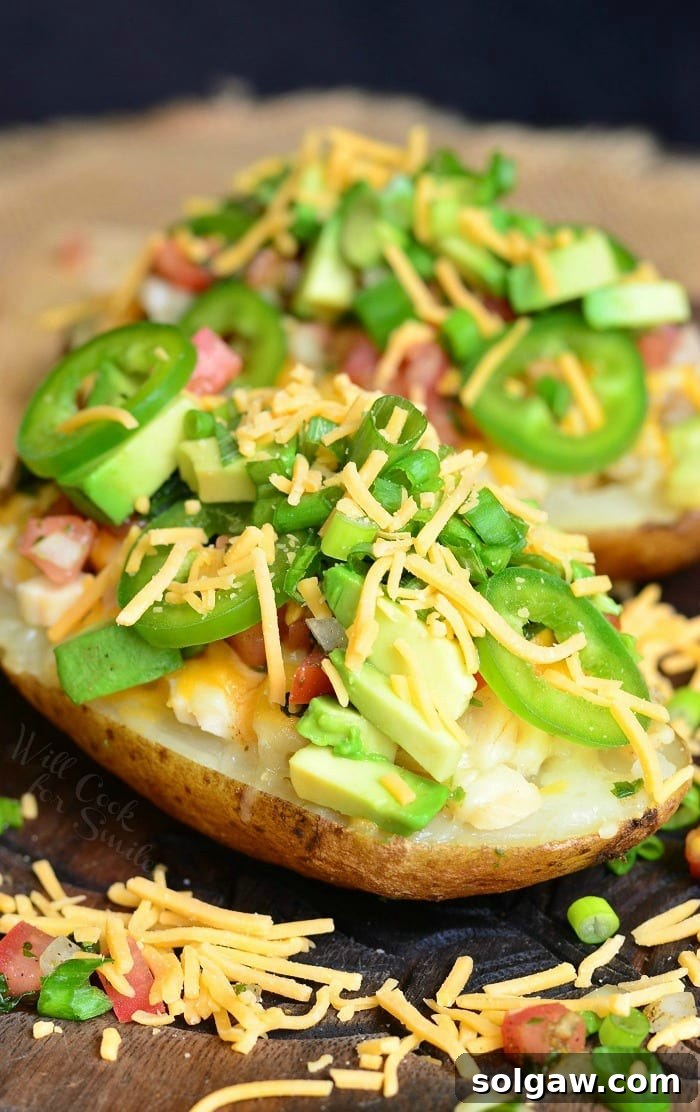 Close up view of fiesta chicken twice baked potatoes on a wooden board topped with chives and sliced jalapenos