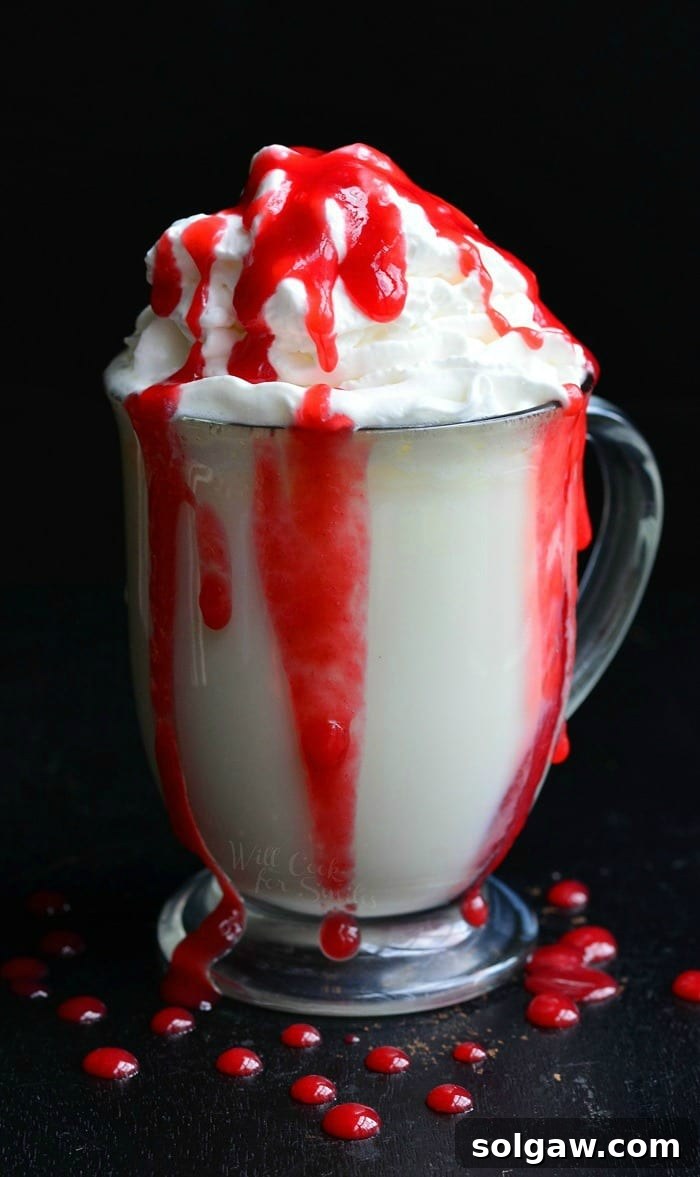 White Chocolate Raspberry Hot Chocolate in a clear glass bowl with whip cream and raspberry sauce on top