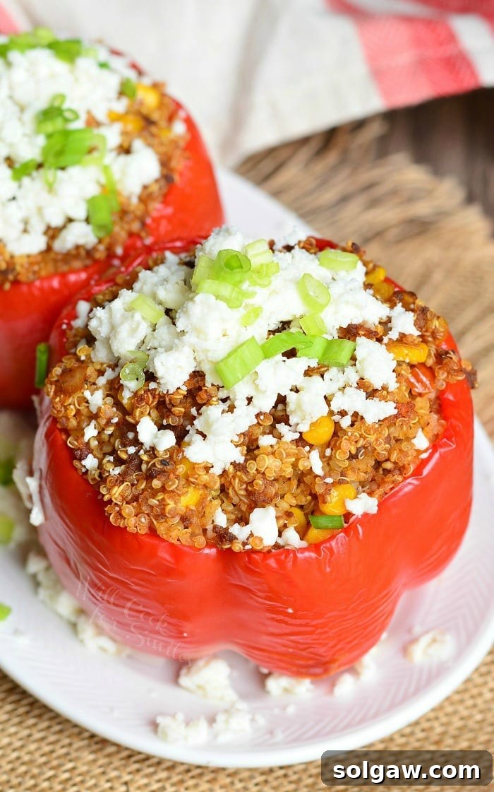 Two chorizo and quinoa stuffed peppers on a white oval plate sitting on a brown placemat on a wooden table as seen from above