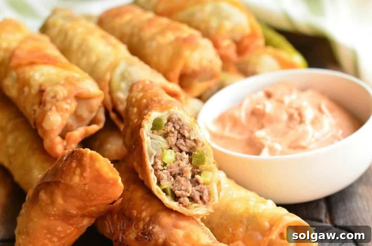 several cheeseburger egg rolls on a board with one cut in half and sauce.