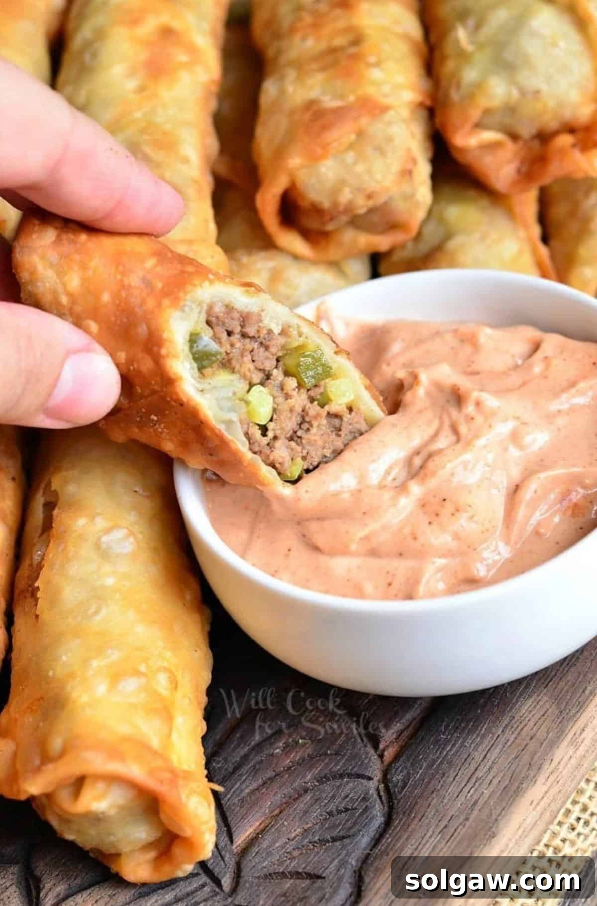 dipping a cut cheeseburger egg roll half into the creamy sauce.