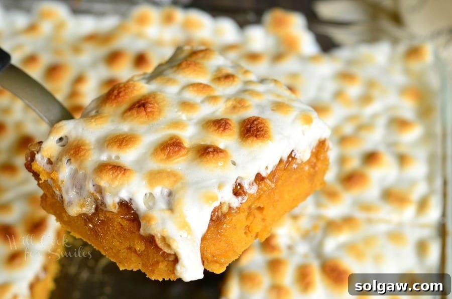 sweet potato casserole with marshmallow topping being lifted out of glass baking pan with a spatula