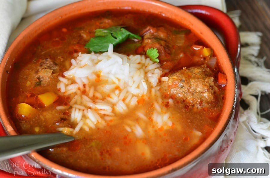 Red clay crock filled with mexican meatballs soup on a white cloth with a spoon in the soup as viewed from above