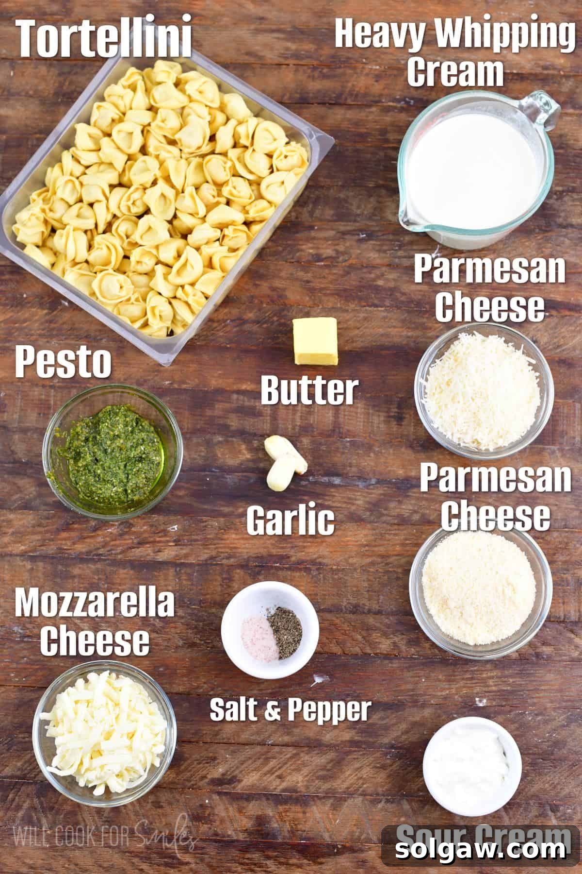 Creamy Pesto Alfredo Tortellini 3 Labeled ingredients for pesto alfredo tortellini on a wood surface, including tortellini, cream, butter, cheeses, garlic, and pesto.