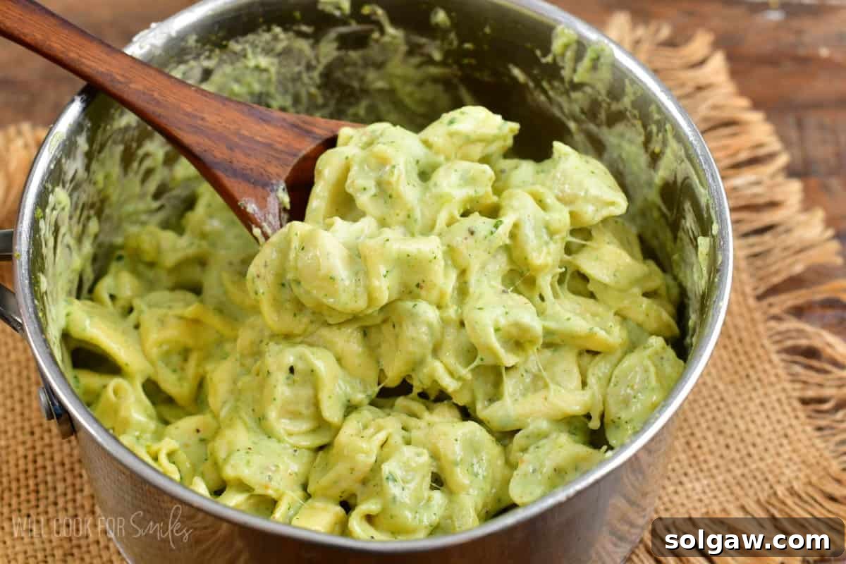 Creamy Pesto Alfredo Tortellini 7 Scooping pesto alfredo tortellini out of the pan with a wooden spoon, ready to be served.