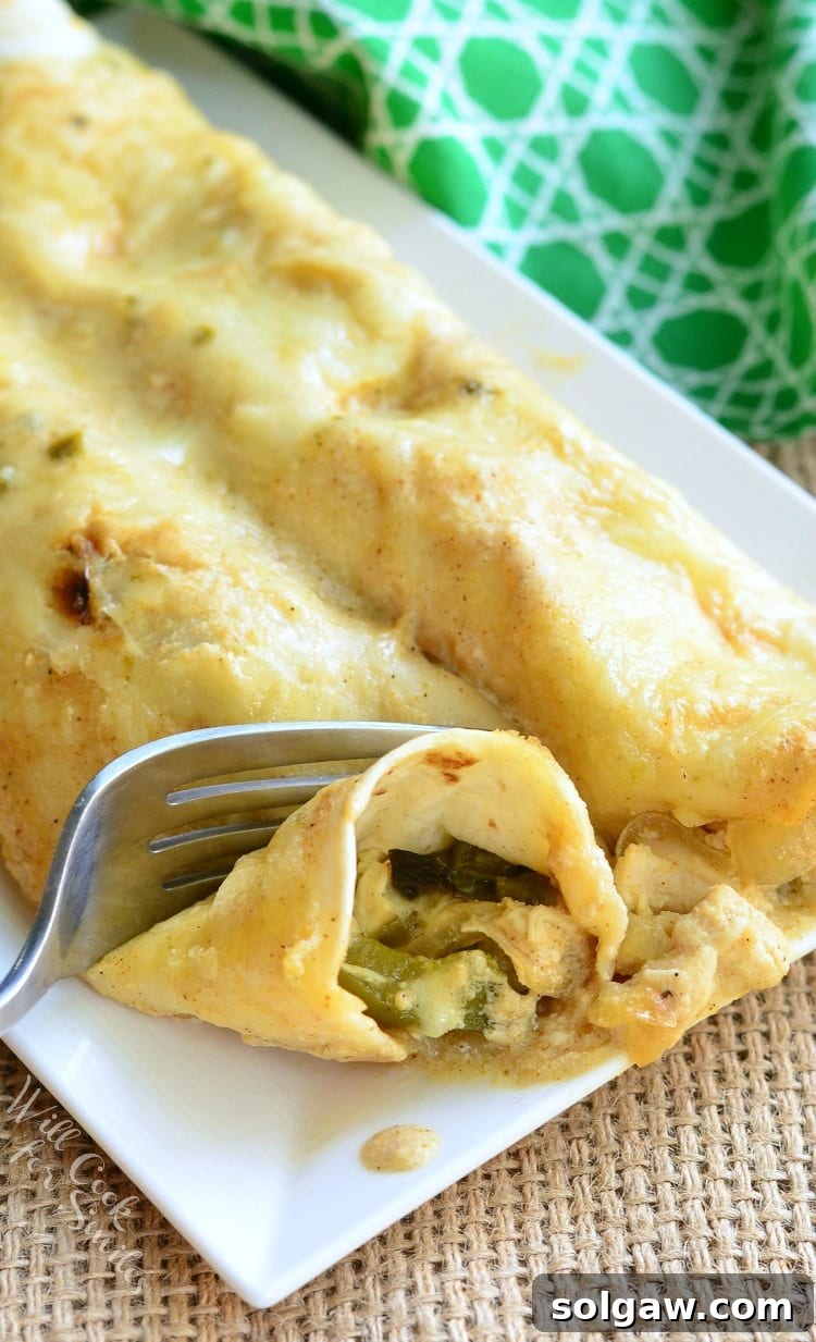 Smoky Poblano Chicken Enchiladas 3 Close-up of a plate of Roasted Poblano and Chicken Enchiladas, with a fork cutting into one.