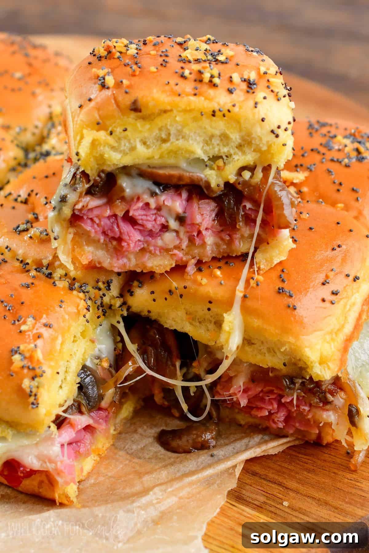 Corned beef sliders on a cutting board, with one slider stacked on top, showcasing the melted cheese and fillings.