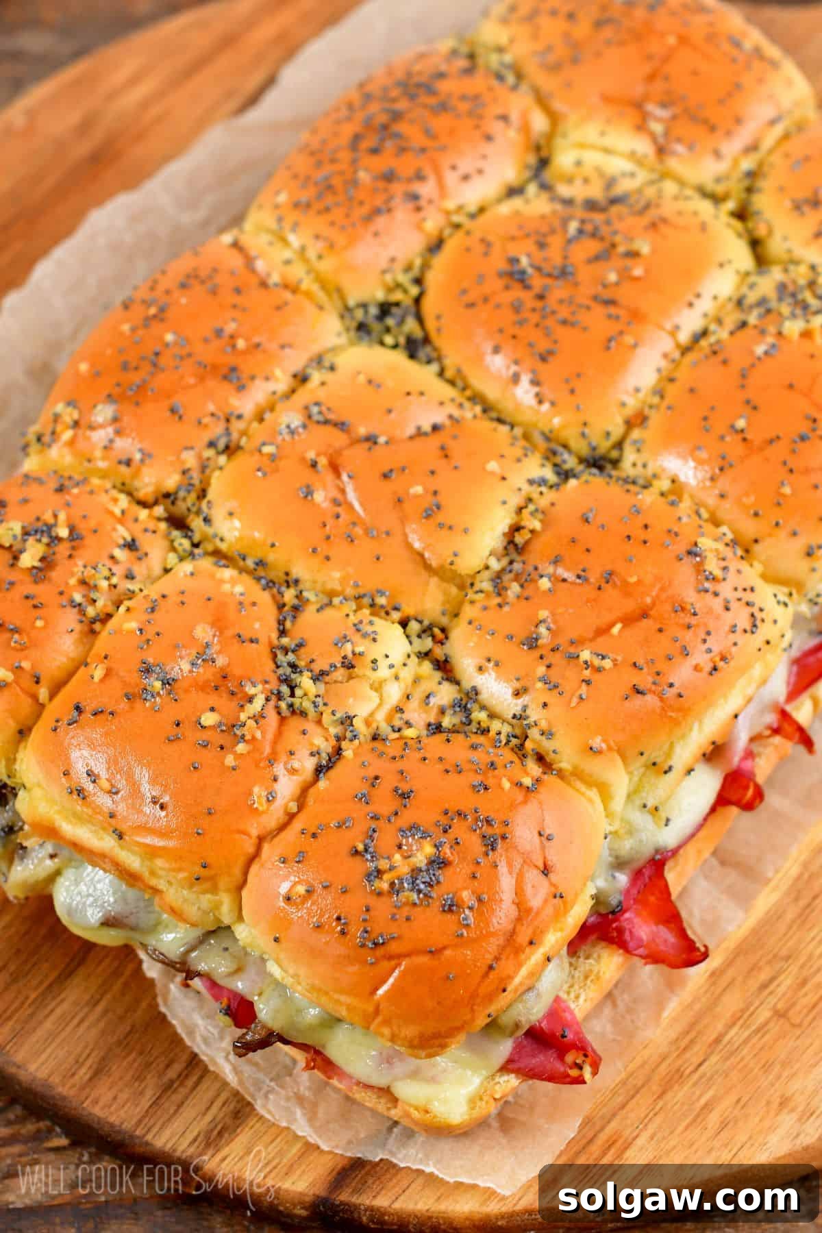 A close-up shot of baked corned beef sliders on a wood cutting board, showcasing the golden-brown rolls and melted Swiss cheese.