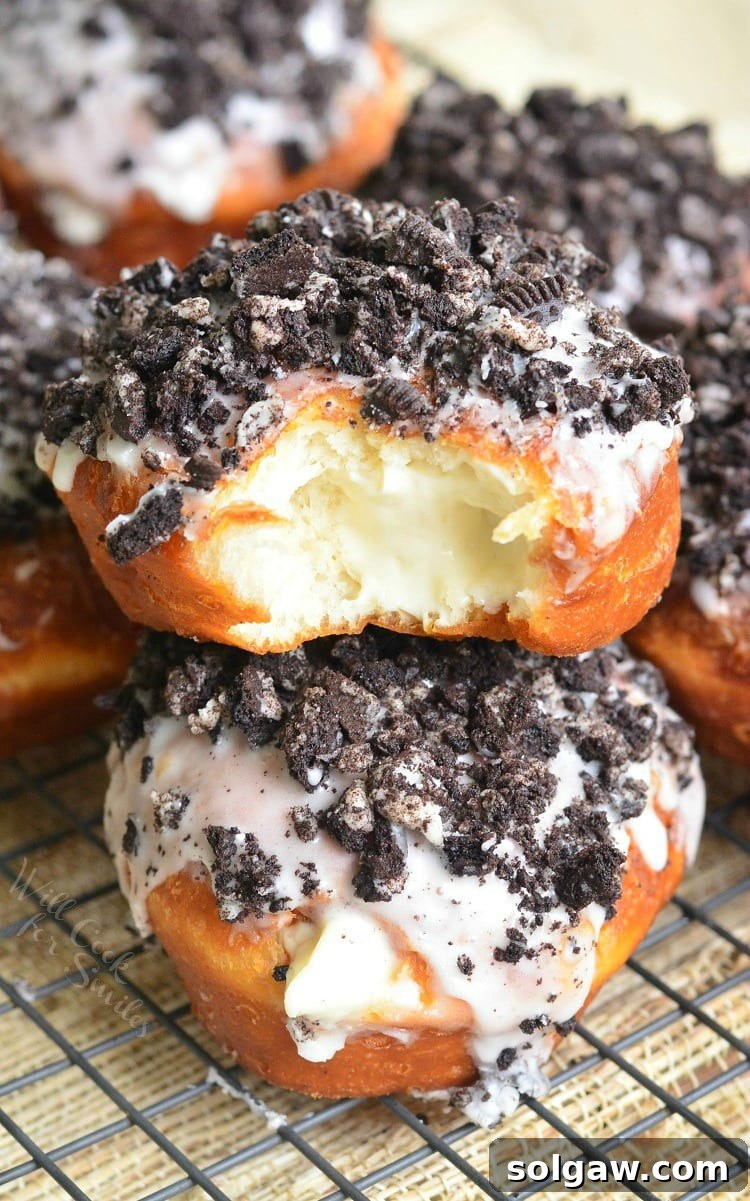 Delicious Oreo Cheesecake Doughnuts with a bite taken out, resting on a cooling rack, drizzled with sweet glaze and crushed Oreo cookies.