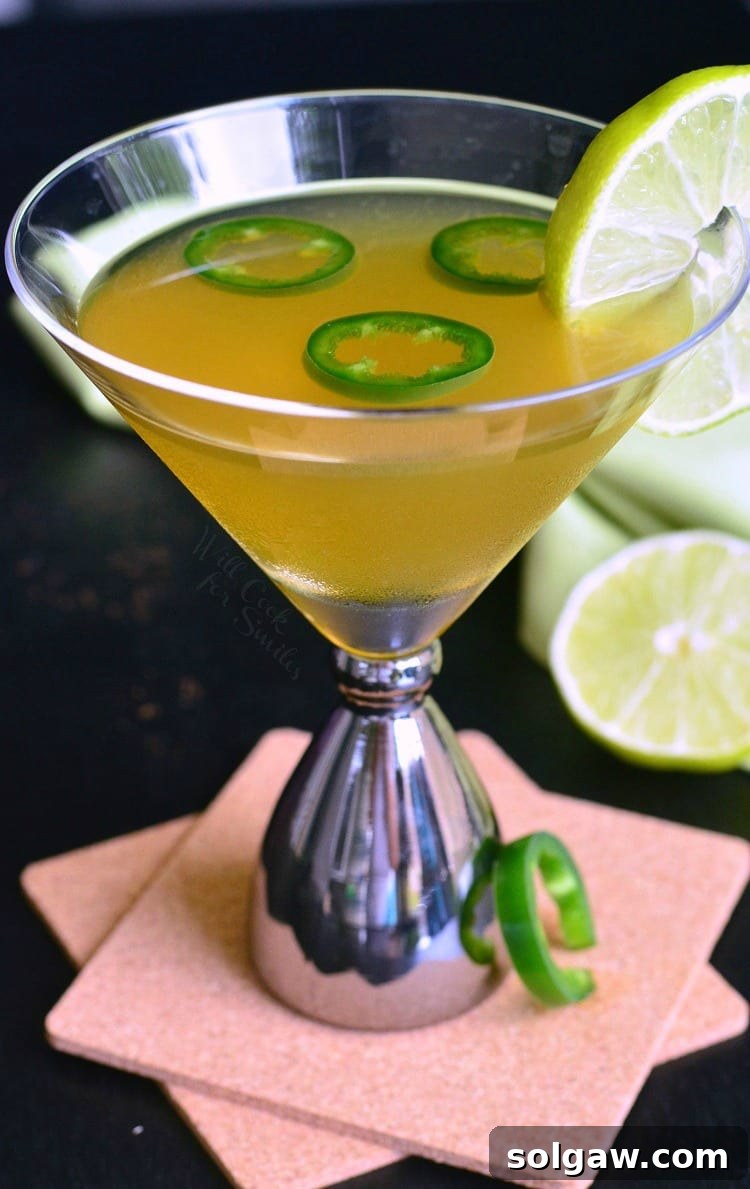 Jalapeno margarita in a martini glass with slices of Jalapeno on top and lime on the side for garnish