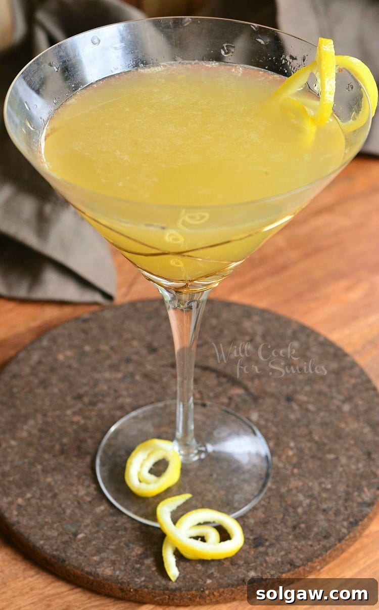 Decorative martini glass filled with pineapple lemon martini with lemon peel garnishes on the rim and around the stem of the glass as viewed from above