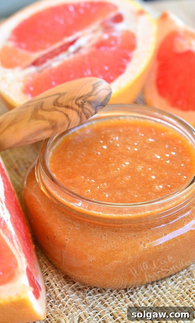 Homemade Grapefruit Sauce in a glass jar with a wooden lid, accompanied by freshly sliced grapefruit, creating a vibrant, appealing display.