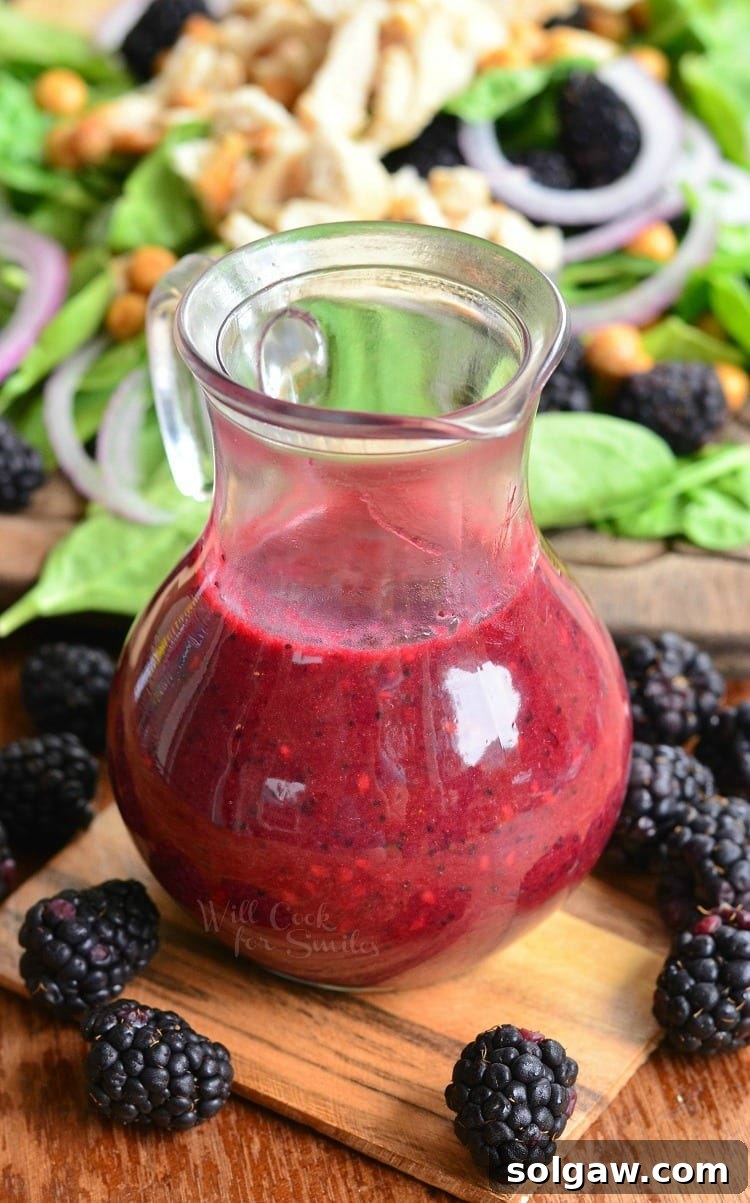 Blackberry Poppy Seed Chicken Spinach Salad 7 Glass of blackberry poppy seed vinaigrette on a wooden board with blackberries scattered around.