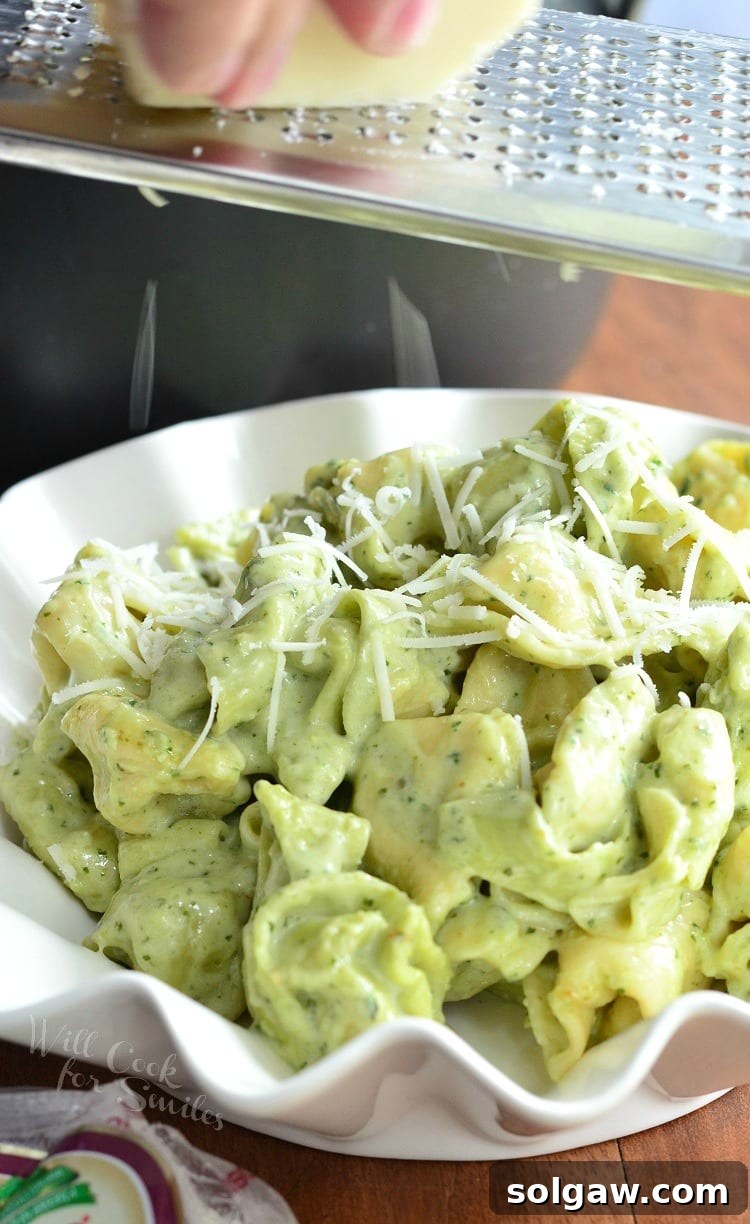 Pesto Alfredo Tortellini served in a white bowl with grated Parmesan cheese.