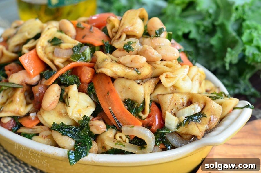 Big oval yellow platter filled with tuscan tortellini salad on a brown placemat with a bottle of oil in the background as viewed close up