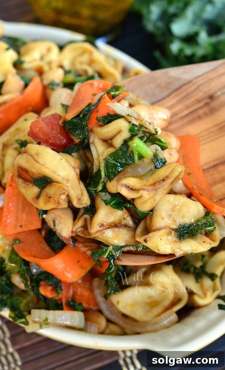 Tuscan Tortellini Salad being scooped with a wooden spoon from a yellow bowl.