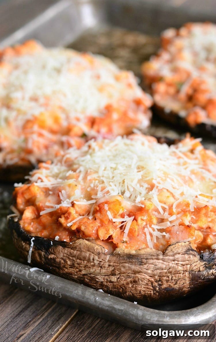 Golden brown Chicken Parmesan Stuffed Portobello mushrooms with melted cheese on a baking sheet