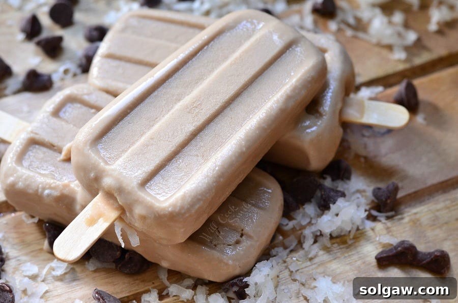 Coconut Mocha Ice Pops stacked up on a cutting board with coconut flakes and chocolate chips 