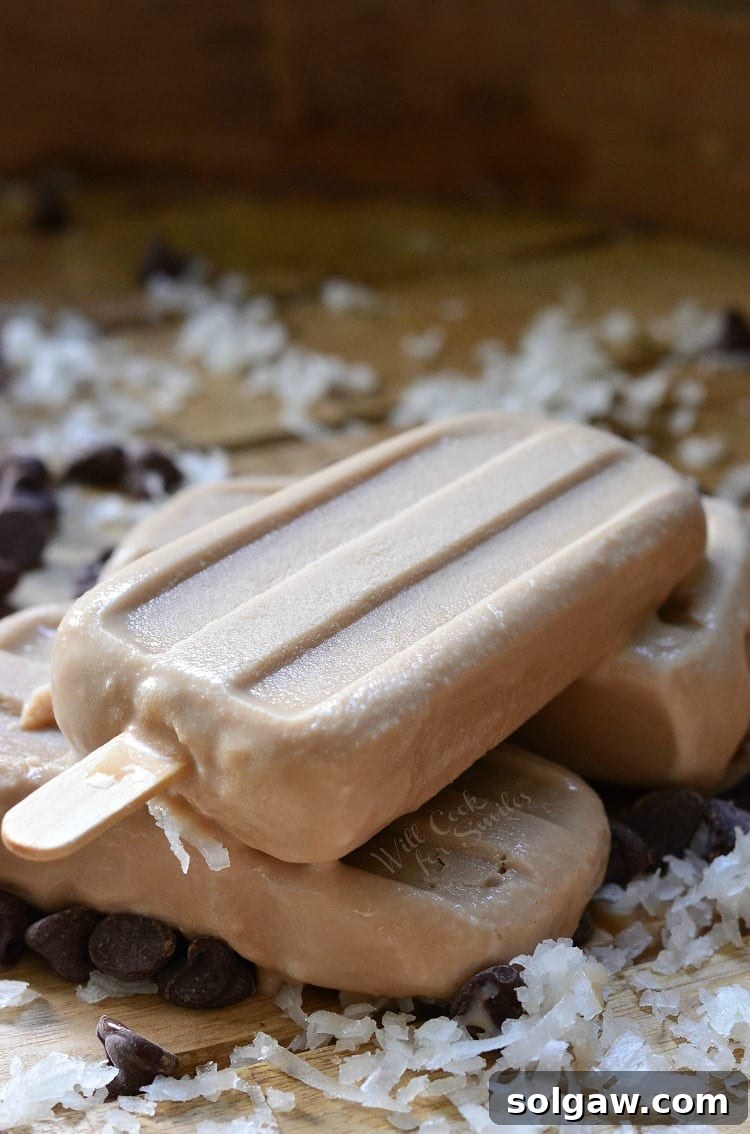 Coconut Mocha Ice Pops stacked up on a cutting board with coconut flakes and chocolate chips 