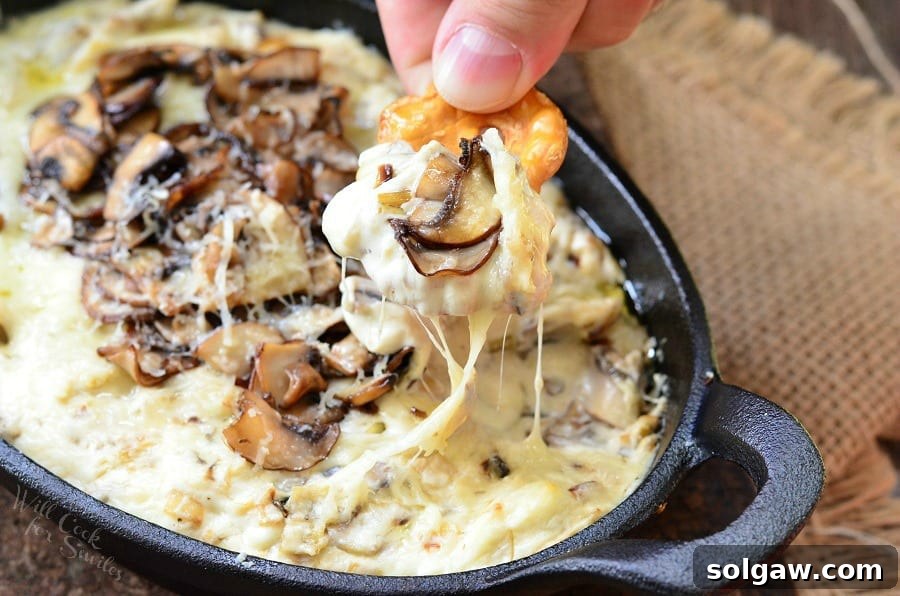 Warm Mushroom Leek Gruyere Cheese Dip 4 Dipping a pretzel into Mushroom Leek and Gruyere Cheese Dip with mushrooms on top in a cast iron pan