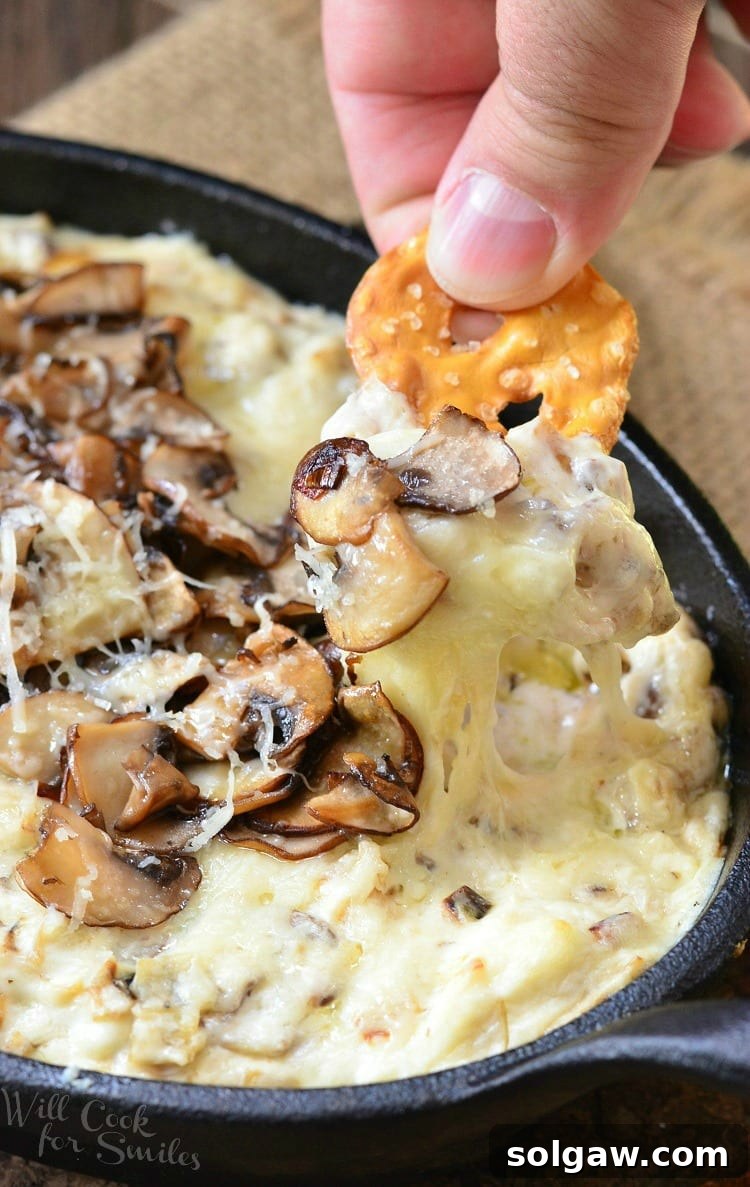 Warm Mushroom Leek Gruyere Cheese Dip 6 Dipping a pretzel into Mushroom Leek and Gruyere Cheese Dip with mushrooms on top in a cast iron pan
