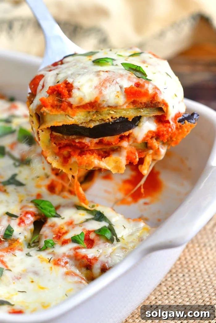 Irresistible Baked Eggplant Parmesan 2 pulling some of the eggplant parmesan out of the baking dish with gooey cheese coming off of the side of the spatula