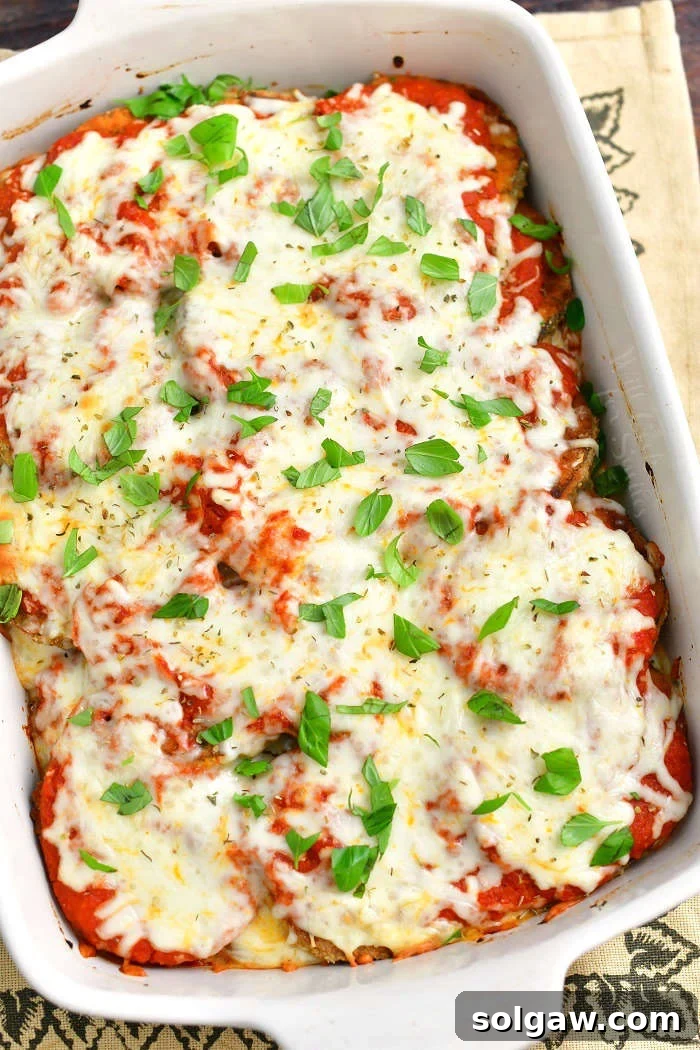 baked eggplant parmesan in a white casserole dish topped with fresh basil leaves and the dish is standing on a burlap towel