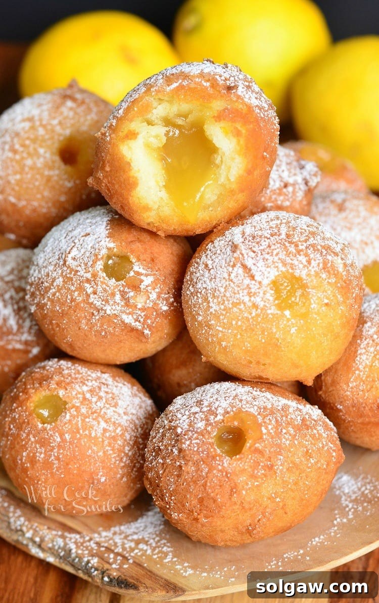 Zesty Lemon Doughnut Poppers 2 Close-up of a stack of golden-brown lemon doughnut holes, with one on top revealing a creamy lemon curd filling through a bite.