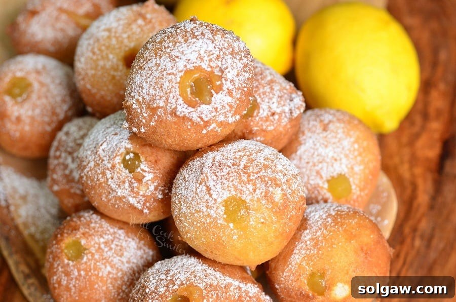 Zesty Lemon Doughnut Poppers 3 Lemon Curd Filled Doughnut Holes stacked elegantly on a plate with a dusting of powdered sugar, with fresh lemon slices in the background.