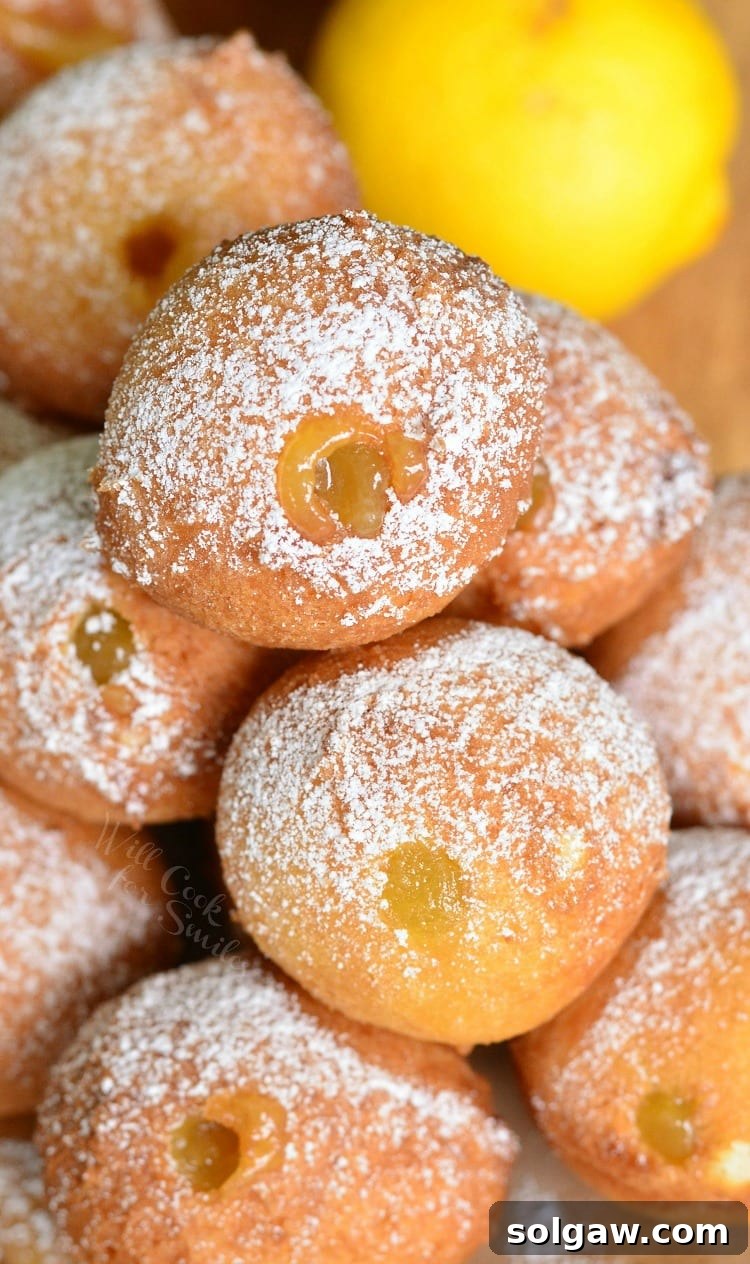 Zesty Lemon Doughnut Poppers 5 Close-up photo of Lemon Curd Filled Doughnut Holes with powdered sugar on top, piled high on a rustic wood plate.