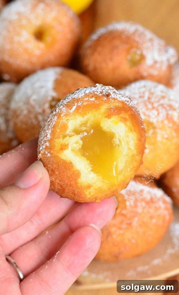 Zesty Lemon Doughnut Poppers 6 Hand holding a Lemon Curd Filled Doughnut with a bite taken out, while other doughnuts are blurred in the background.