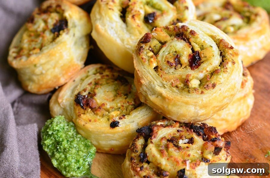 Tuscan Pesto Chicken Pinwheels 4 Pesto Chicken and Sun Dried Tomato Pinwheels on a cutting board with a spoon of pesto
