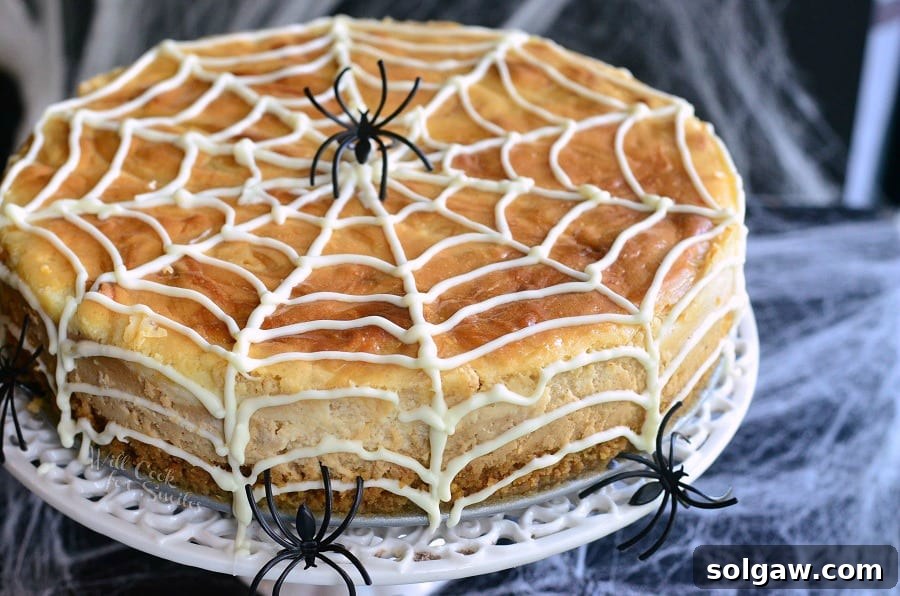 Spiderweb Swirl White Chocolate Peanut Butter Cheesecake 4 cheesecake on a white cake stand with spider web made out of frosting on it and 3 spiders