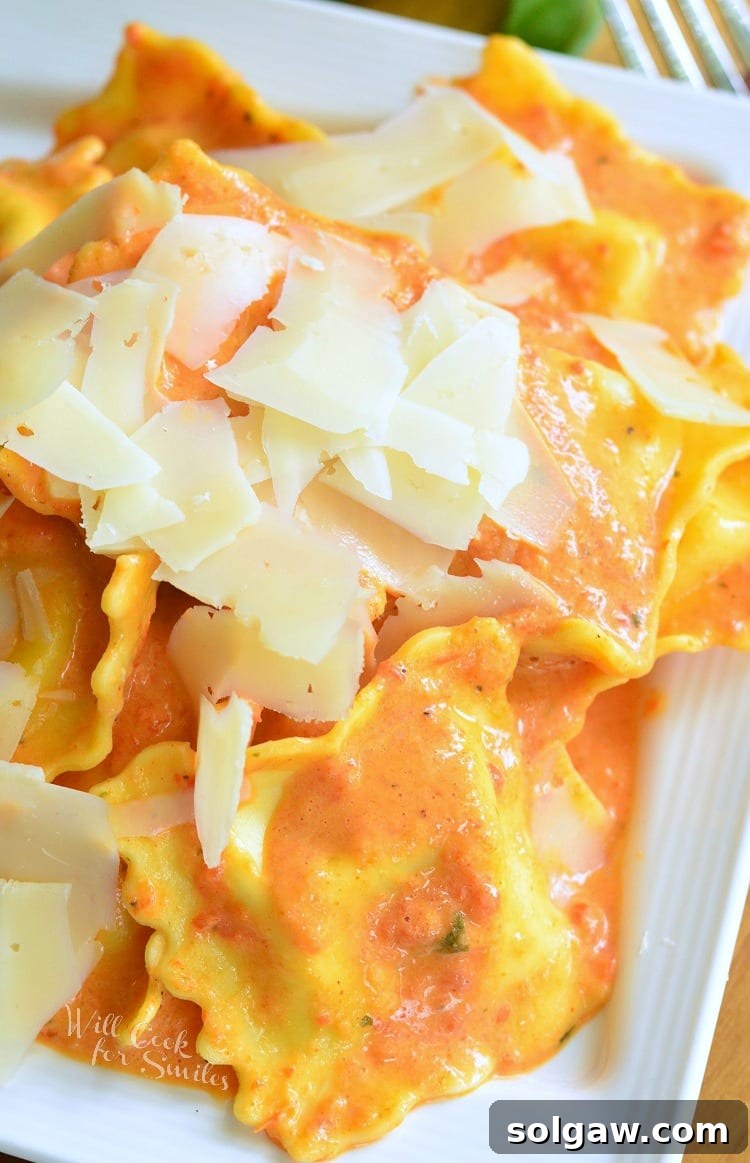 Top view of Ravioli in a creamy red bell pepper and basil sauce topped with shaved Parmesan cheese on a white plate