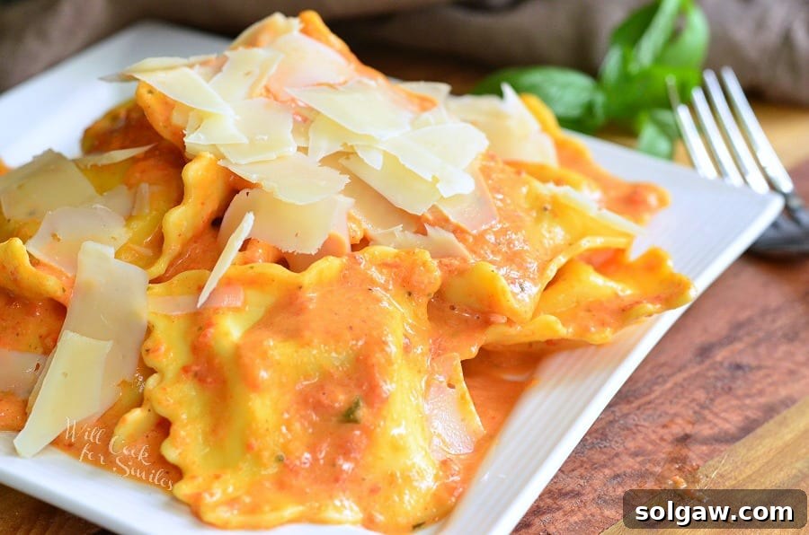 Ravioli in a creamy red bell pepper and basil sauce topped with shaved Parmesan cheese on a white plate