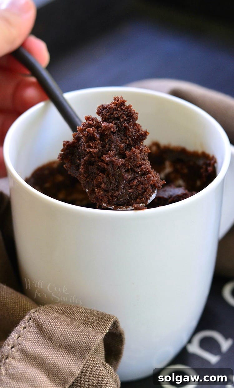 Chocolate cake in a white coffee mug with a spoon lifting some out 