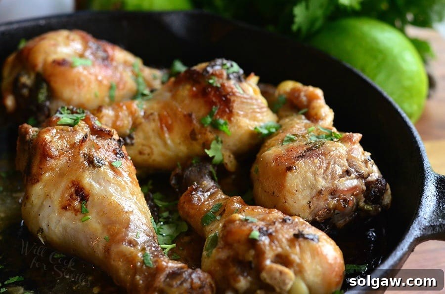 Coconut Lime Chicken Drumsticks cooking in a rustic cast iron pan, surrounded by lime wedges and fresh cilantro.