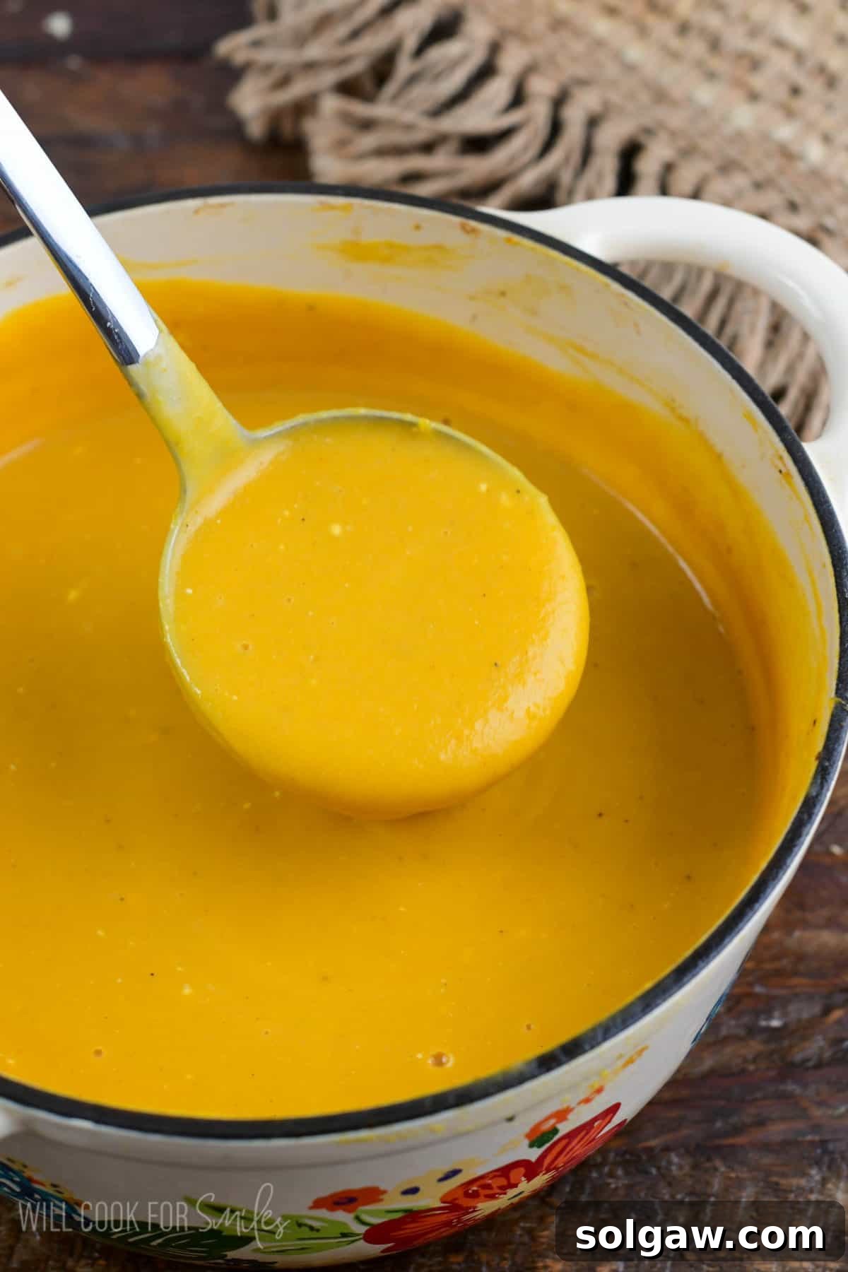 A ladle expertly scooping a serving of Butternut Squash Potato Soup from a charming flower pot, highlighting its rich texture.