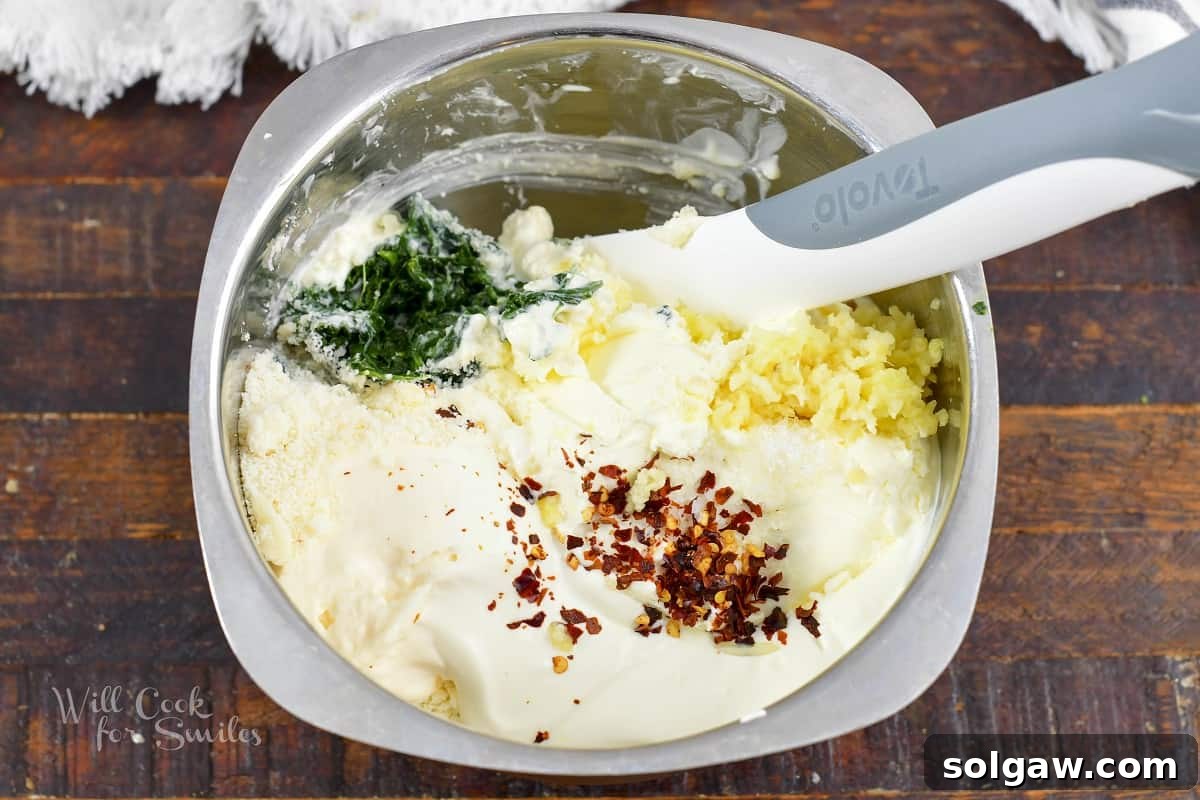 All spinach dip ingredients, including cream cheese, sour cream, mayo, and spinach, gathered in a large mixing bowl.