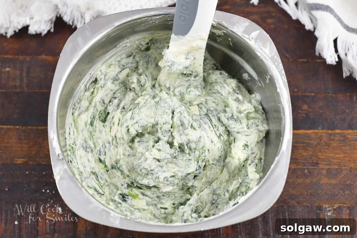 Close-up of spinach dip ingredients being mixed thoroughly in a metal bowl with a spatula.
