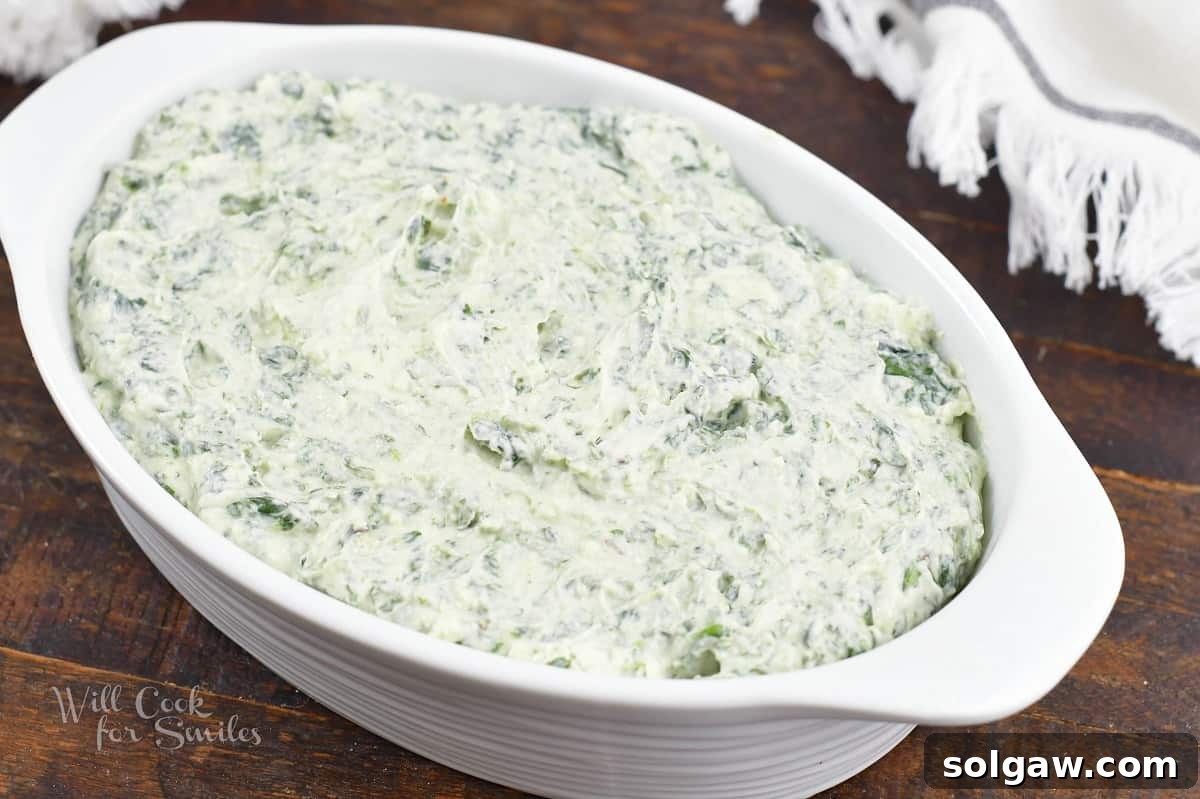 The smooth spinach dip mixture evenly spread in a white baking dish, ready for the oven.