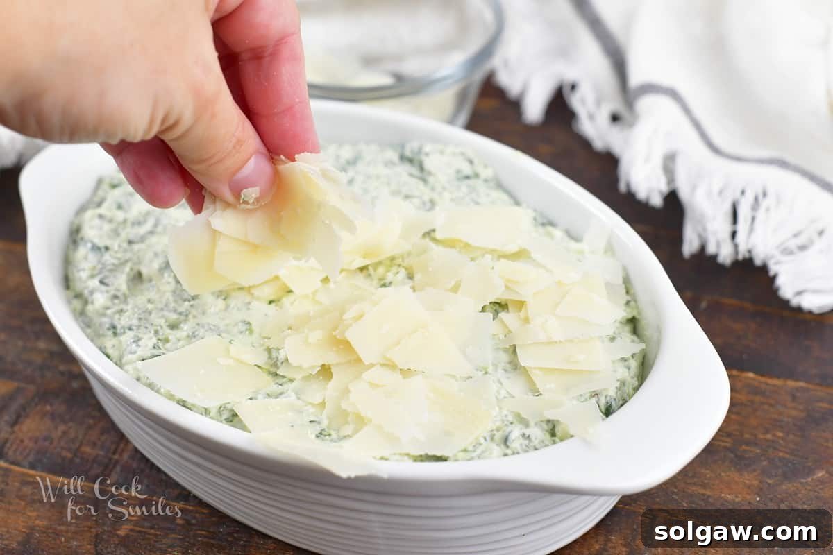 Shaved Parmesan cheese being sprinkled over the spinach dip mixture in a baking dish before baking.