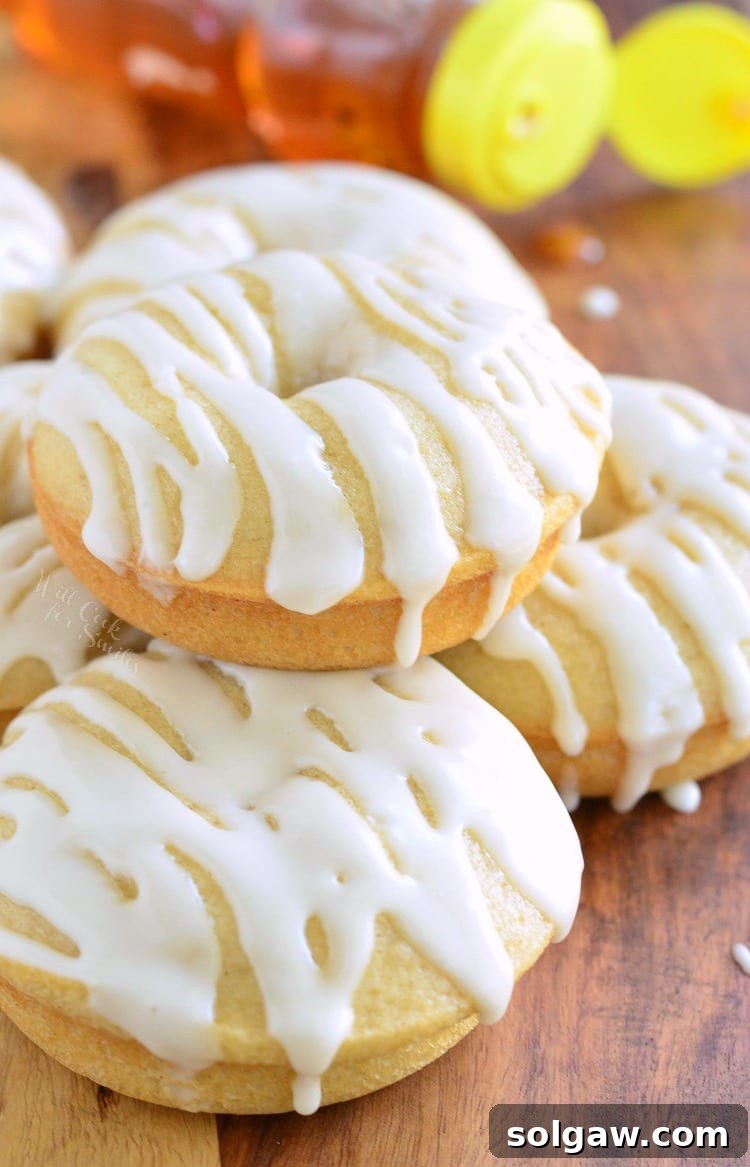 Golden Honey Delights 2 Stacked baked honey doughnuts on a rustic wooden cutting board with a honey bear bottle in the soft-focus background, highlighting their golden color and delicate texture.