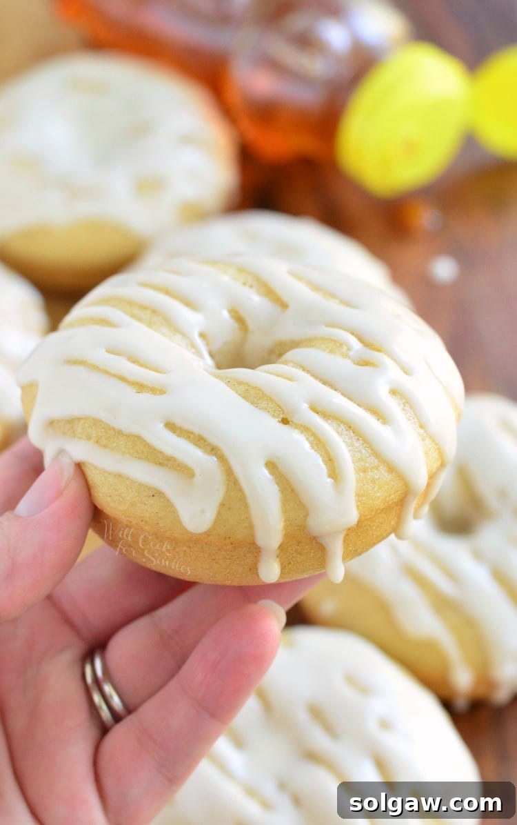 Golden Honey Delights 3 Close-up shot of a hand holding a perfectly glazed baked honey doughnut, showing its soft texture and inviting golden-brown hue.