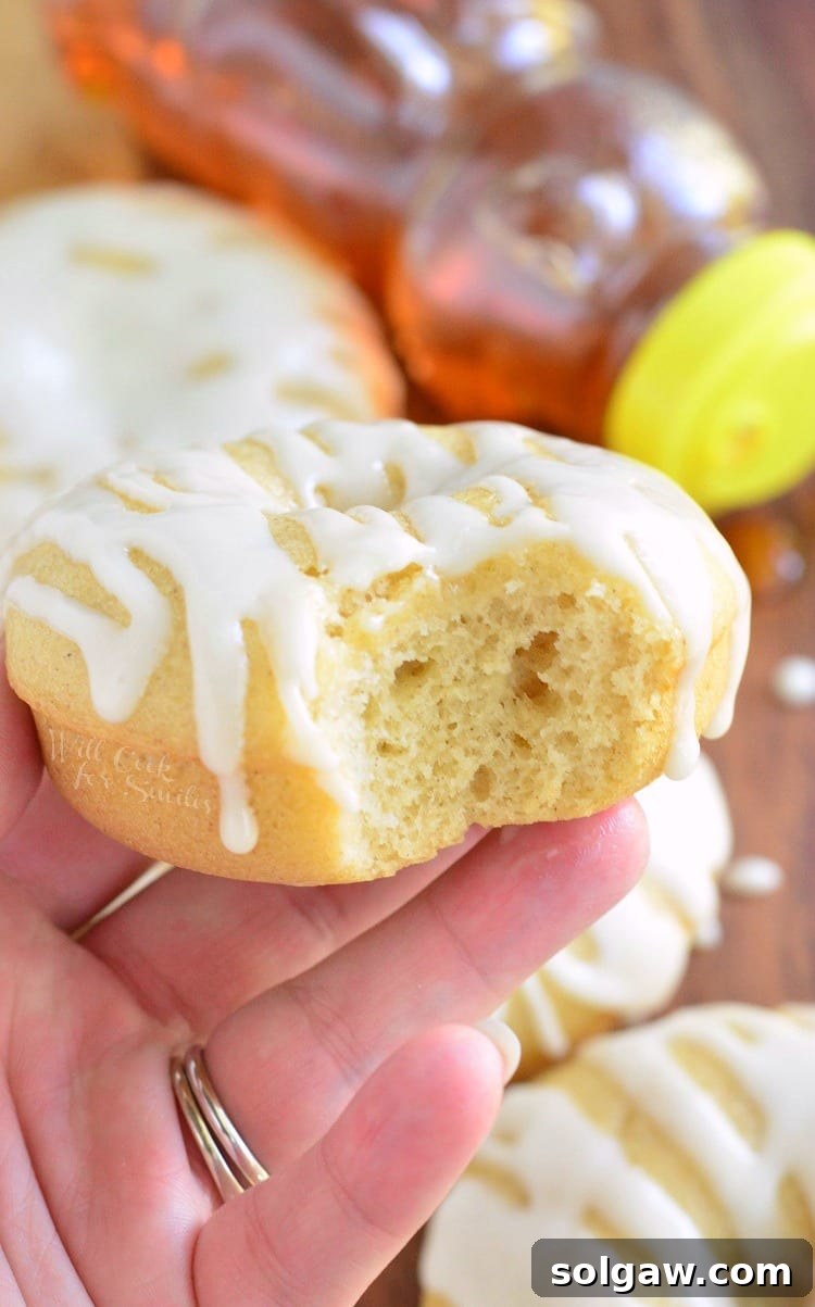 Golden Honey Delights 6 Close-up shot of a hand holding a freshly baked honey doughnut with a bite taken out, revealing its soft, fluffy interior and the luscious honey glaze.