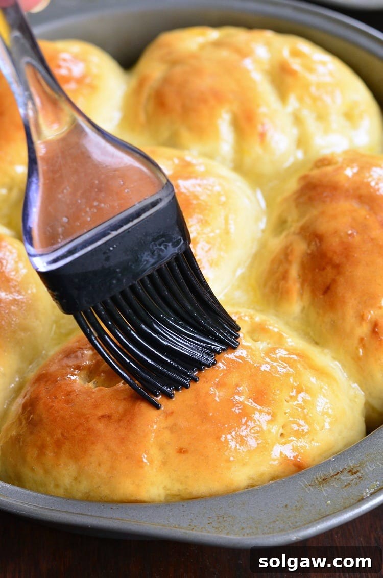 Brushing warm Honey Lemon Dinner Rolls with butter glaze in a baking dish