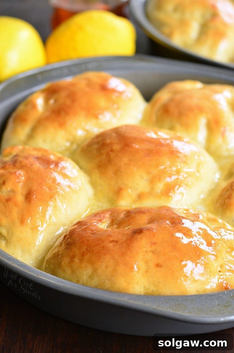 Honey Lemon Dinner Rolls in a baking dish with fresh lemons in the background, a beautiful culinary scene