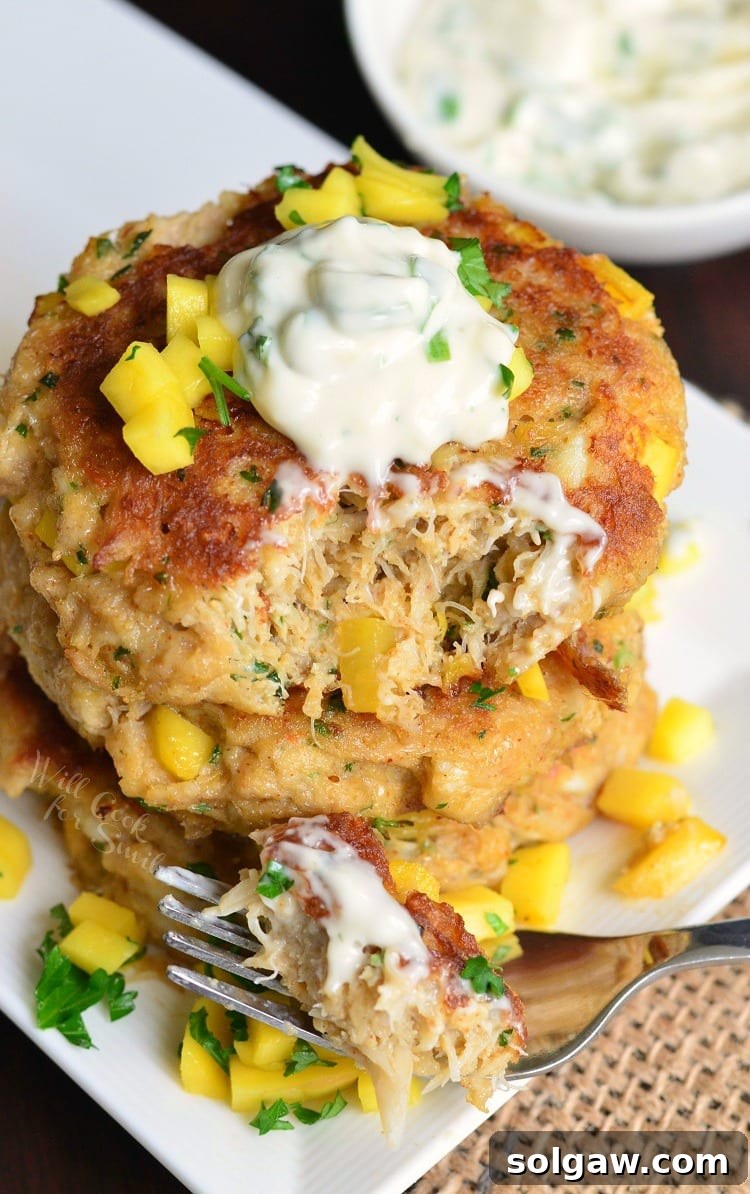 top view of Spicy Mango Crab Cakes stacked on a plate with sour cream on top and diced mango and parsley on the plate  with a fork 